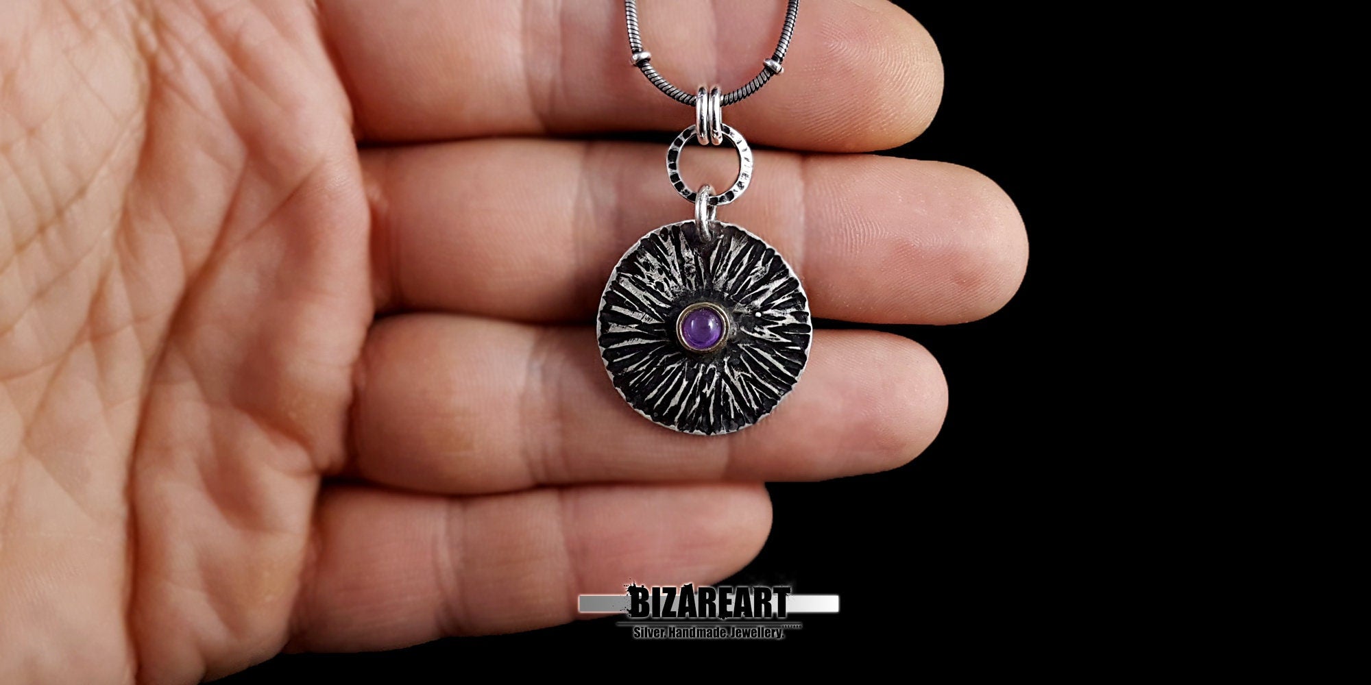 Lifestyle scale shot showing the Bromo Charm pendant held in a hand to demonstrate its 5-gram weight and physical size relative to a person.