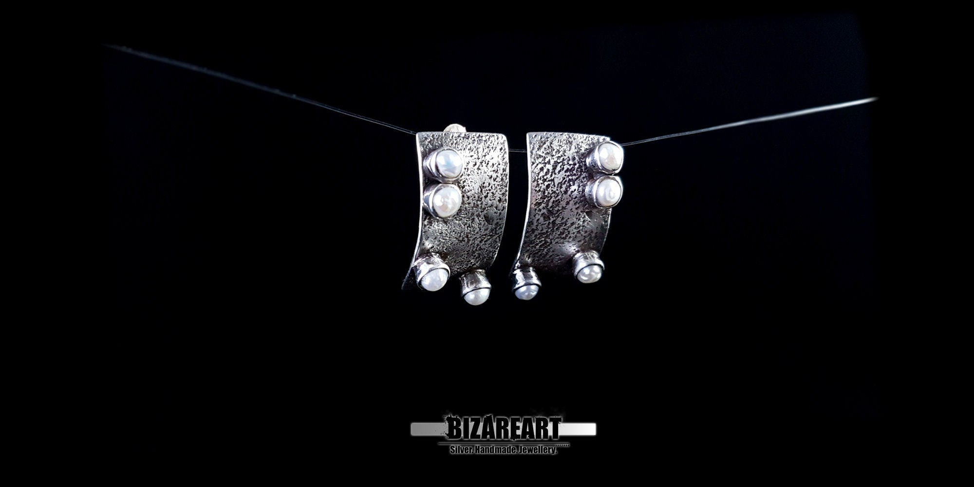 Close-up of the curved, sculptural design of the silver earrings, highlighting how they catch the light.