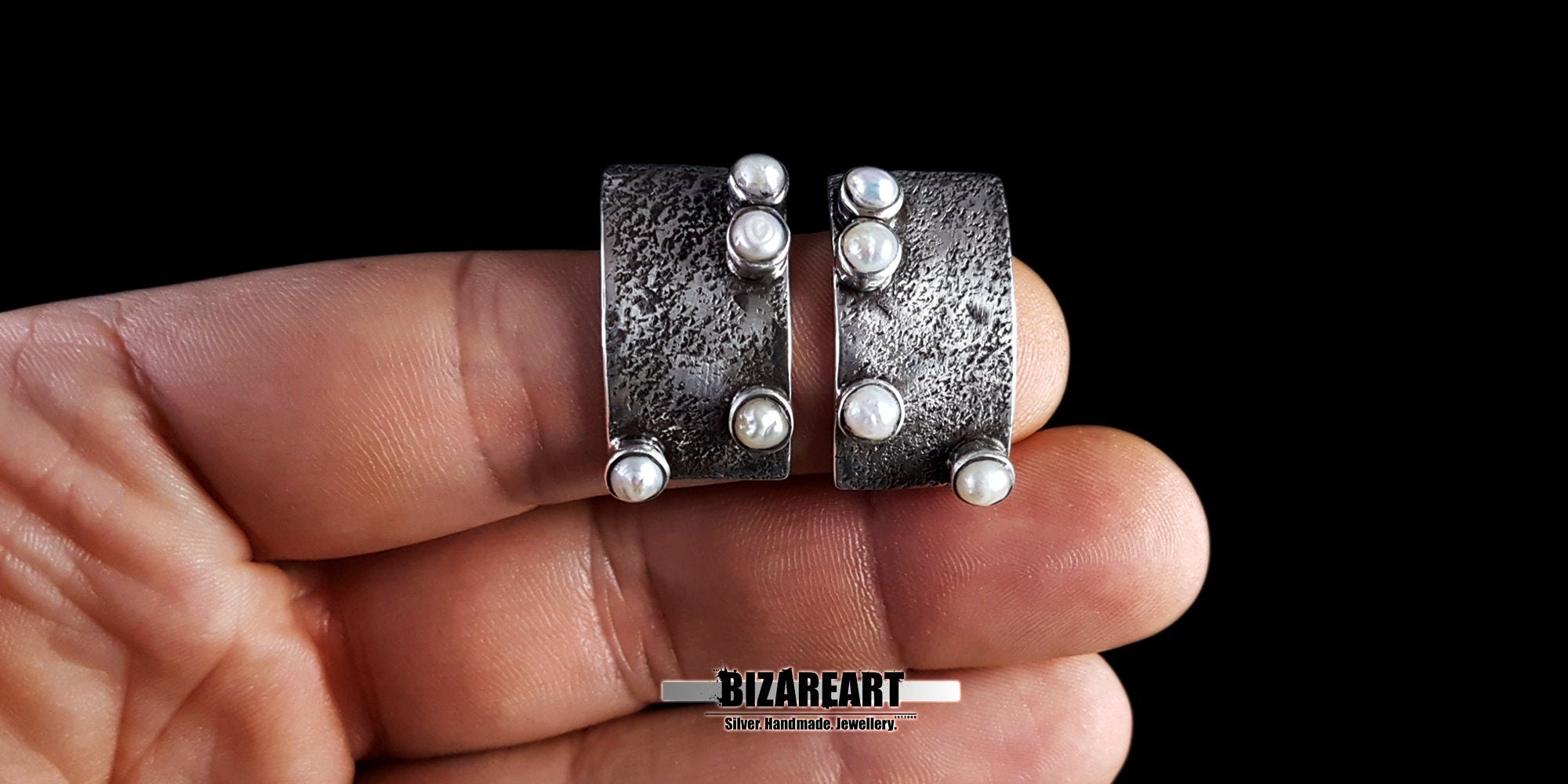Close-up of the textured silver and pearl studs resting on fingers for a clear size comparison.