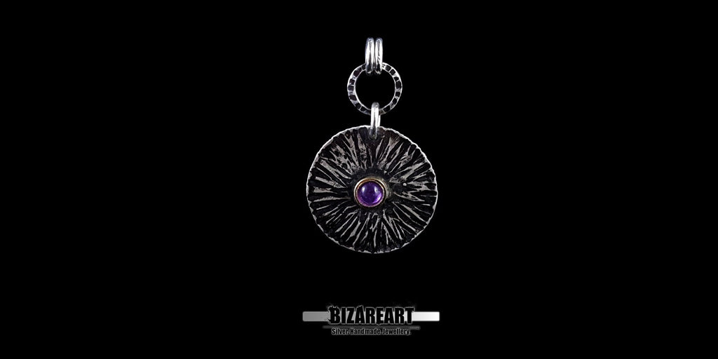 Front view of the Bromo Charm pendant featuring radial "Sea of Sand" etchings and a central amethyst stone set in a bronze bezel.