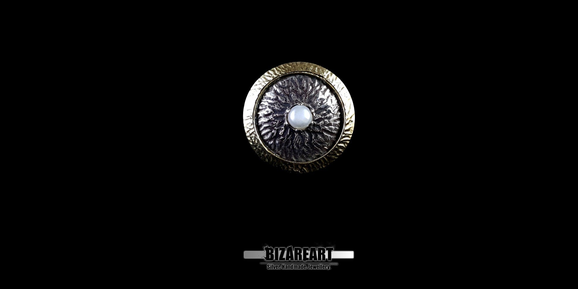 Top-down view of the Bromo Ring featuring a central freshwater pearl, oxidized silver crater texture, and a gold-plated bronze outer rim against a black background.
