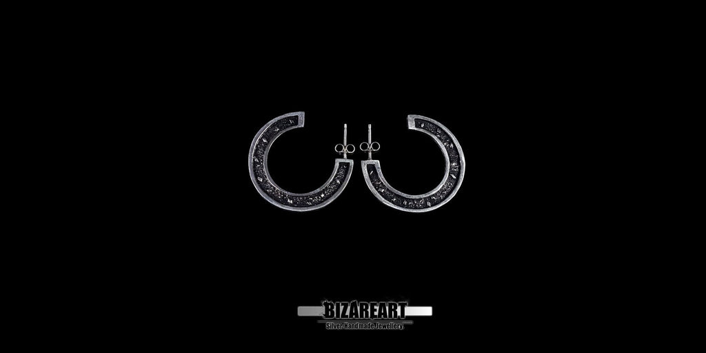 A pair of circular sector sterling silver stud earrings featuring intricate granulation textures and dark oxidation, displayed against a high-contrast black background.