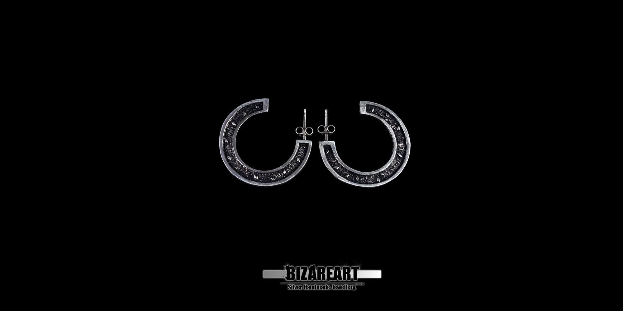 A pair of circular sector sterling silver stud earrings featuring intricate granulation textures and dark oxidation, displayed against a high-contrast black background.