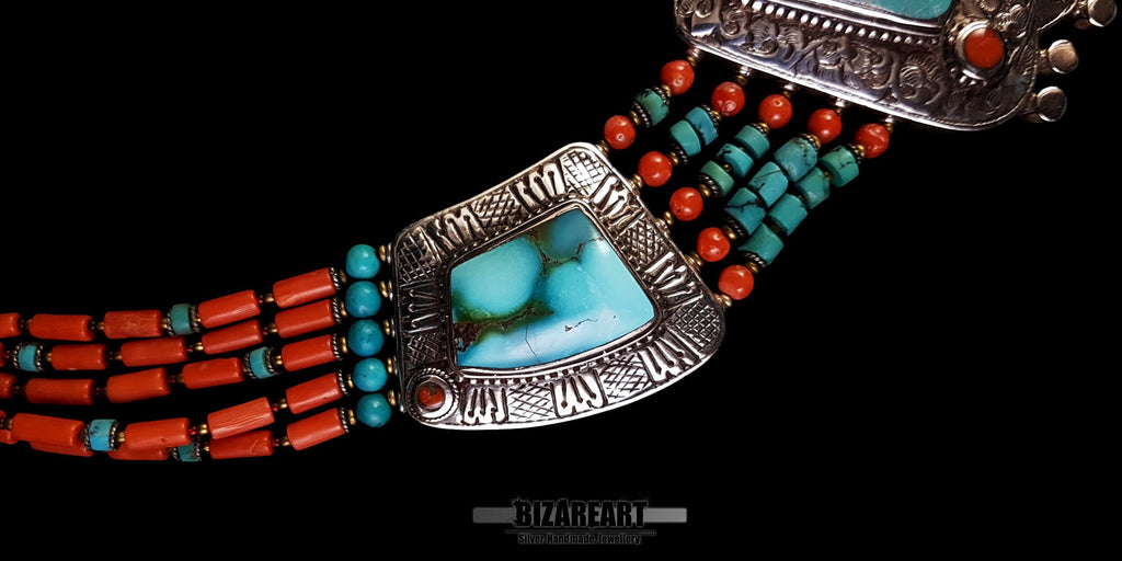 close up 360-degree angle of the vintage Tibetan silver necklace, zooming in on the intricate turquoise sidepiece, red coral strands, and artisan metalwork details against a black background.