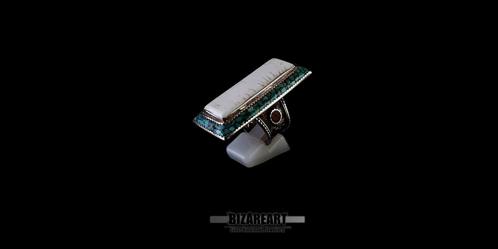 Angled side view of a large handcrafted Tibeto-Nepalese silver ring featuring an elongated white conch cabochon, turquoise inlay border, and a bezel-set red coral stone on the shank, displayed on a ring stand against a black background.