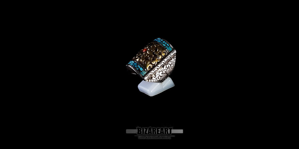 Handmade Tibetan-Nepalese silver and bronze statement ring with Himalayan Turquoise mosaic and central Red Coral, displayed on a white stand against a black background.