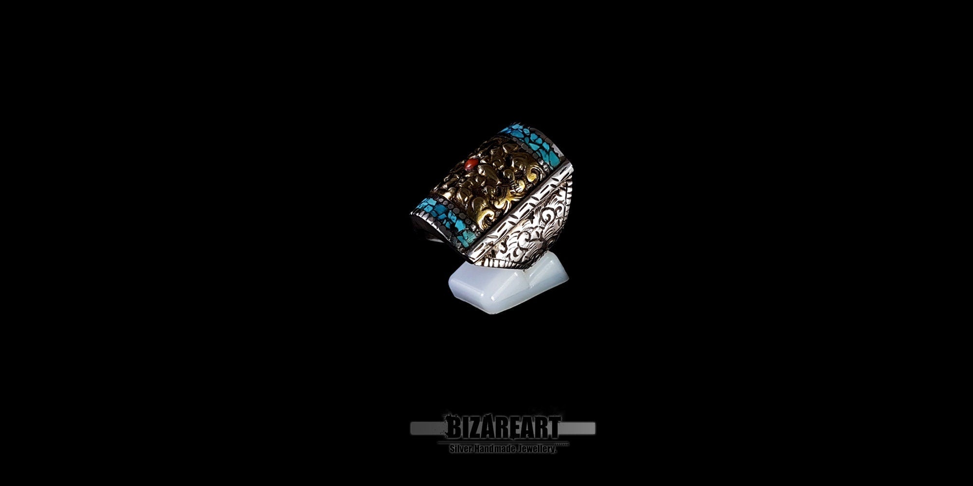 Handmade Tibetan-Nepalese silver and bronze statement ring with Himalayan Turquoise mosaic and central Red Coral, displayed on a white stand against a black background.