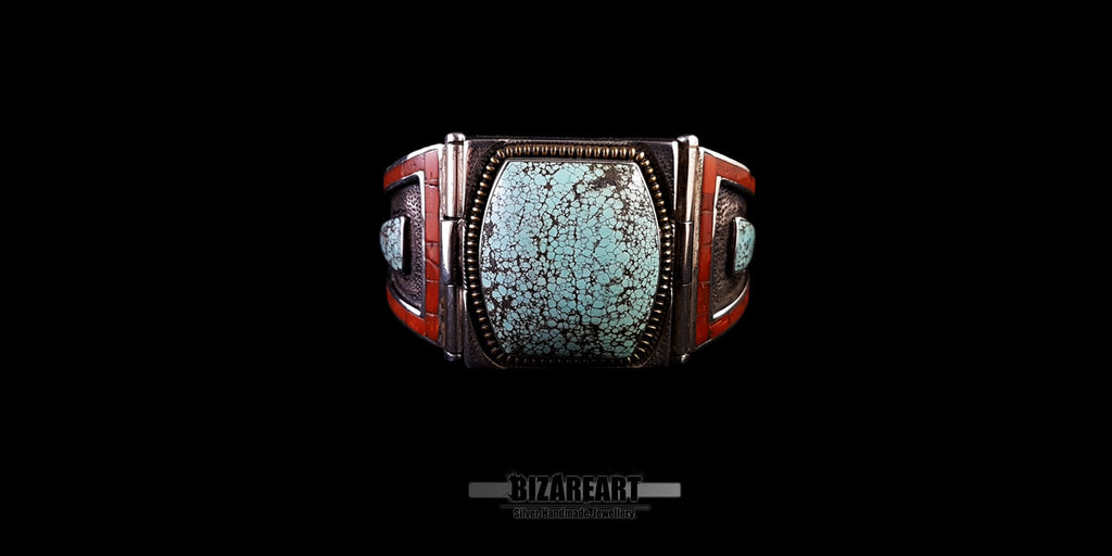 Front close-up of a handmade Tibetan-style silver cuff bracelet featuring a large, rectangular matrix turquoise stone. The centerpiece is flanked by two panels of inlaid red coral mosaic and smaller turquoise details.