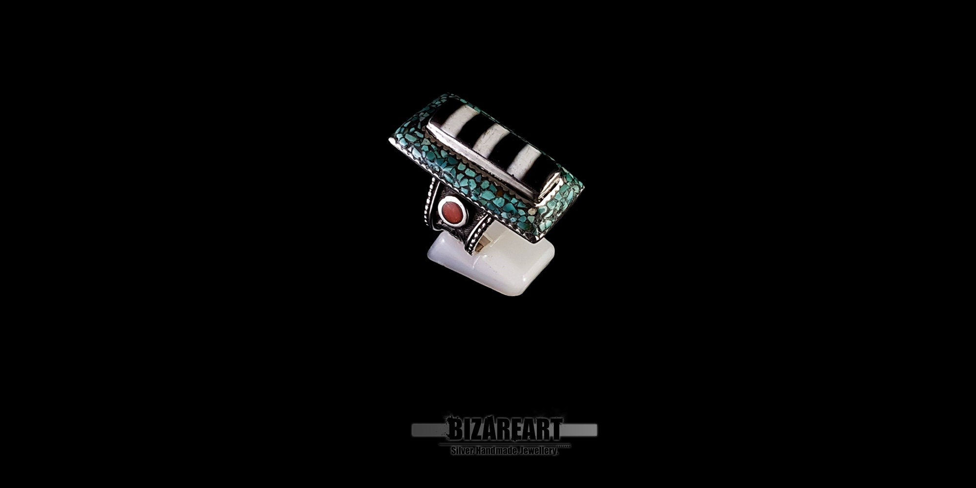Angled front view of a vintage Tibeto-Nepalese silver statement ring featuring a striped agate center, turquoise mosaic, and red coral on a white display stand, by Bizareart.