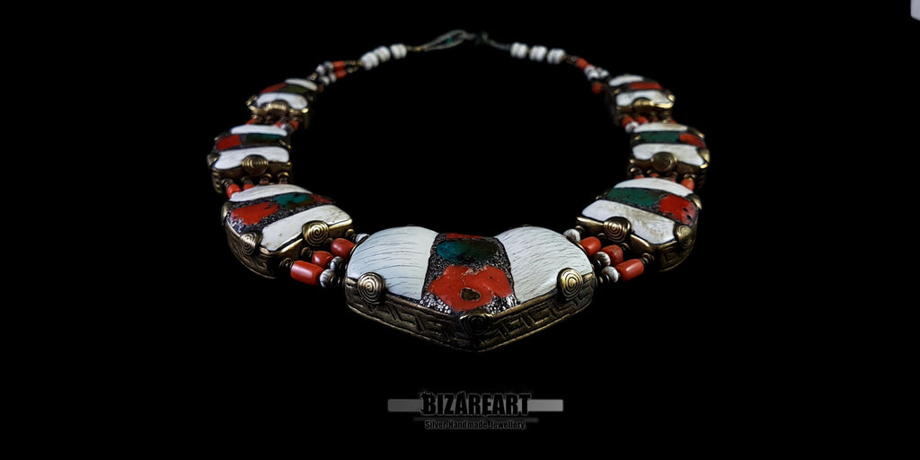 Angled front view of a vintage Nepalese necklace featuring a large inlaid bronze pendant, white Tibetan conch shell segments, and vibrant red coral and turquoise stones against a black background.