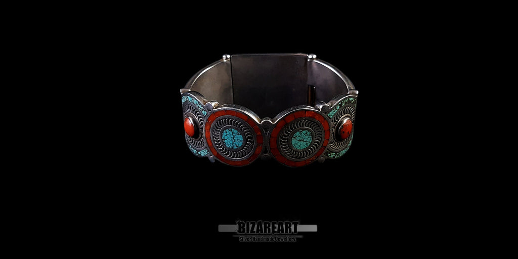 A direct back view of the closed bracelet cuff, highlighting the decorative rear silver plate which features additional small turquoise and red coral settings and intricate wirework. Set against a black background.