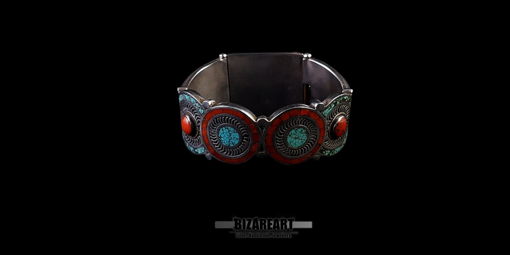 A direct back view of the closed bracelet cuff, highlighting the decorative rear silver plate which features additional small turquoise and red coral settings and intricate wirework. Set against a black background.