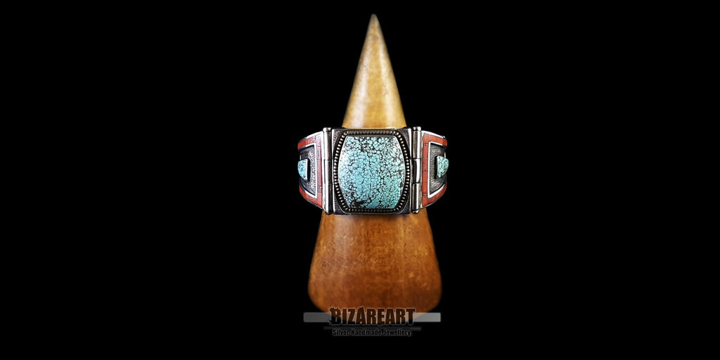 The silver cuff bracelet displayed on a turned wooden jewelry stand. This view showcases the complete circumference and the full color contrast of the turquoise and coral in a 3D perspective.
