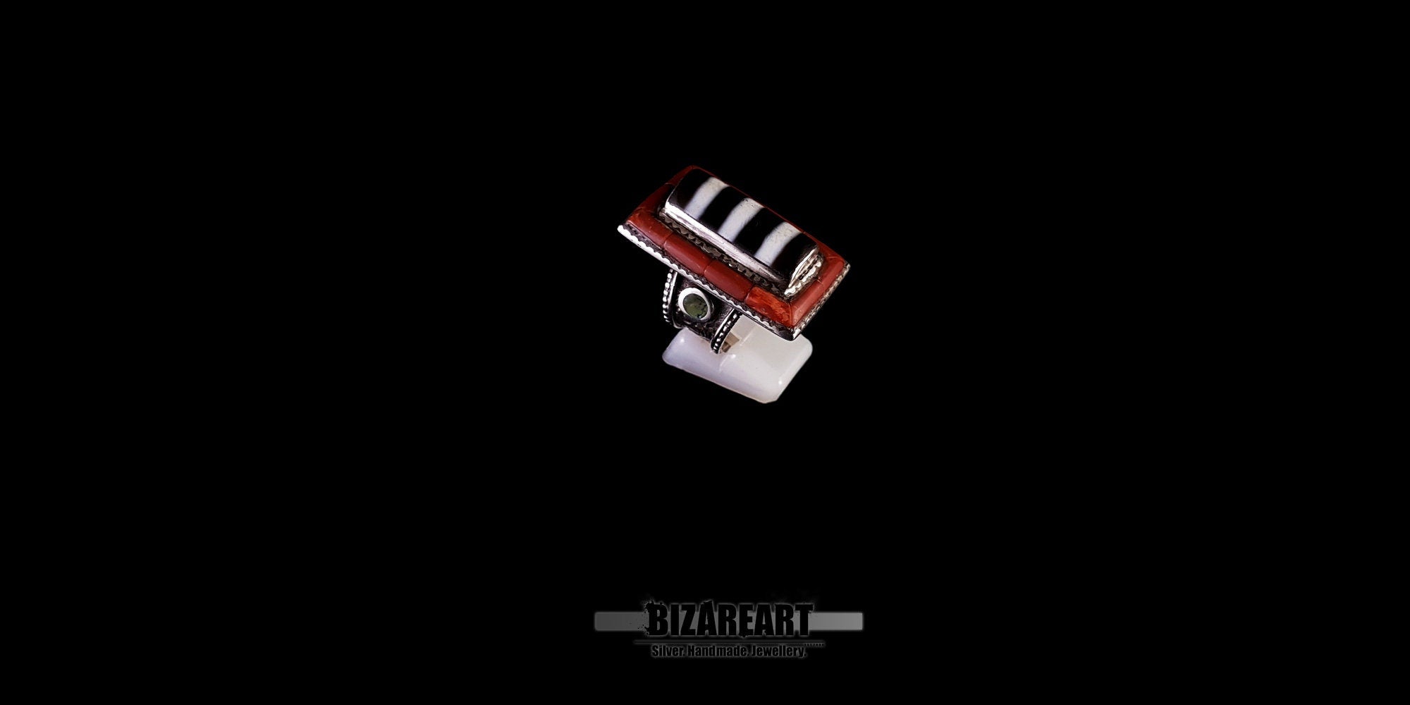 Three-quarter angled view of a handmade vintage Nepalese ring in silver, showcasing the raised tiered design with striped agate and red coral mosaic on a black background.