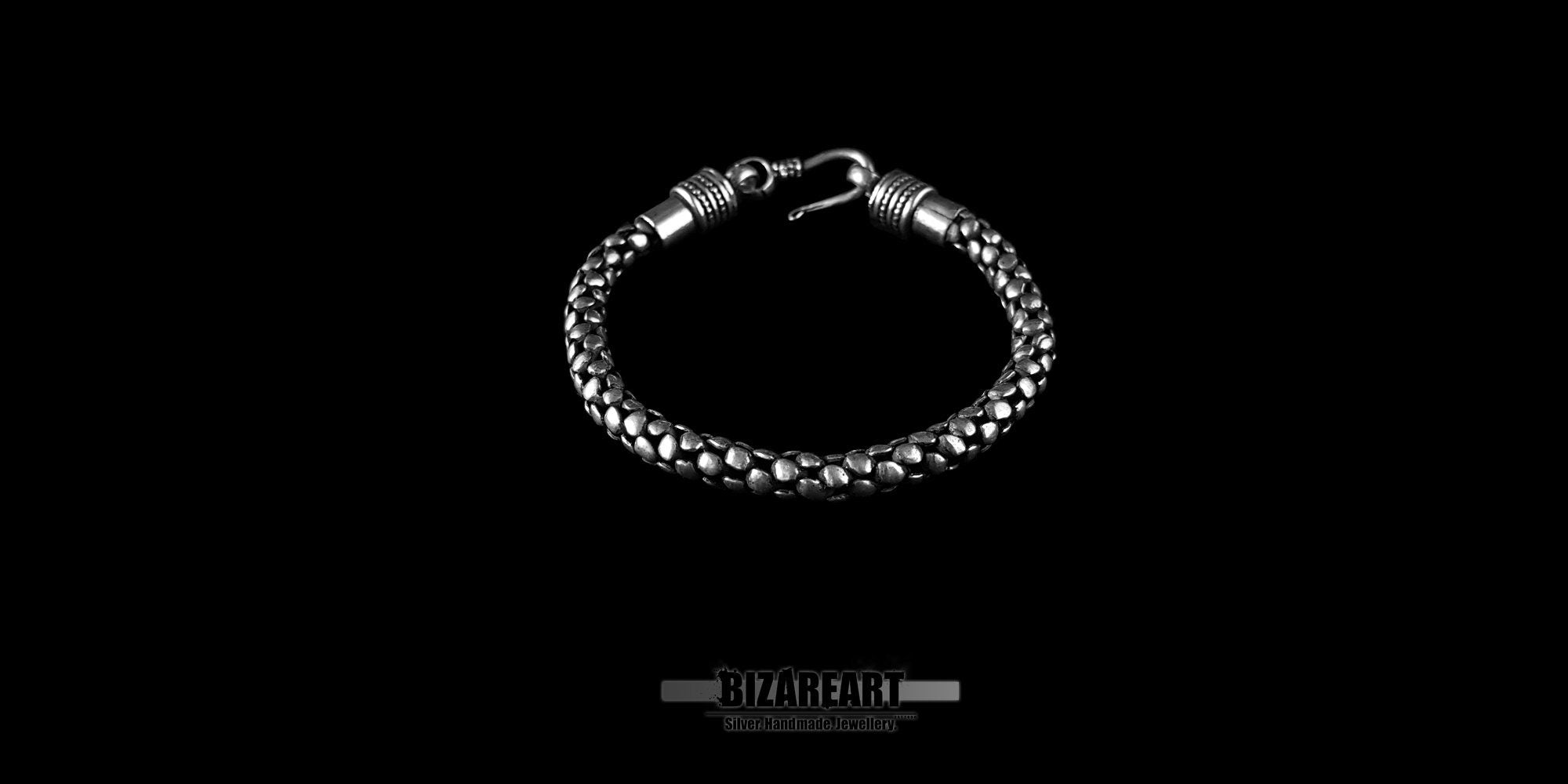 Close-up view of a textured silver bracelet with handcrafted pewter links displayed on a black cushion.