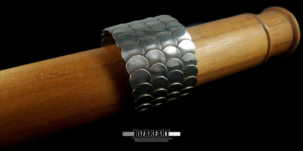 A close-up side view of the bracelet worn on a wooden pole, highlighting the texture and the way the scales overlap.