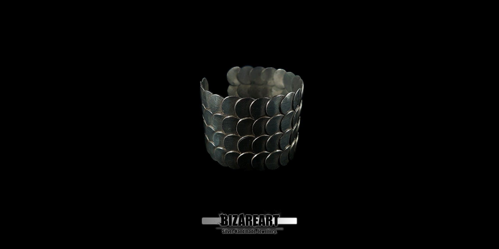 A front-facing view of the silver cuff bracelet showing its cylindrical shape and the uniform rows of silver scales.