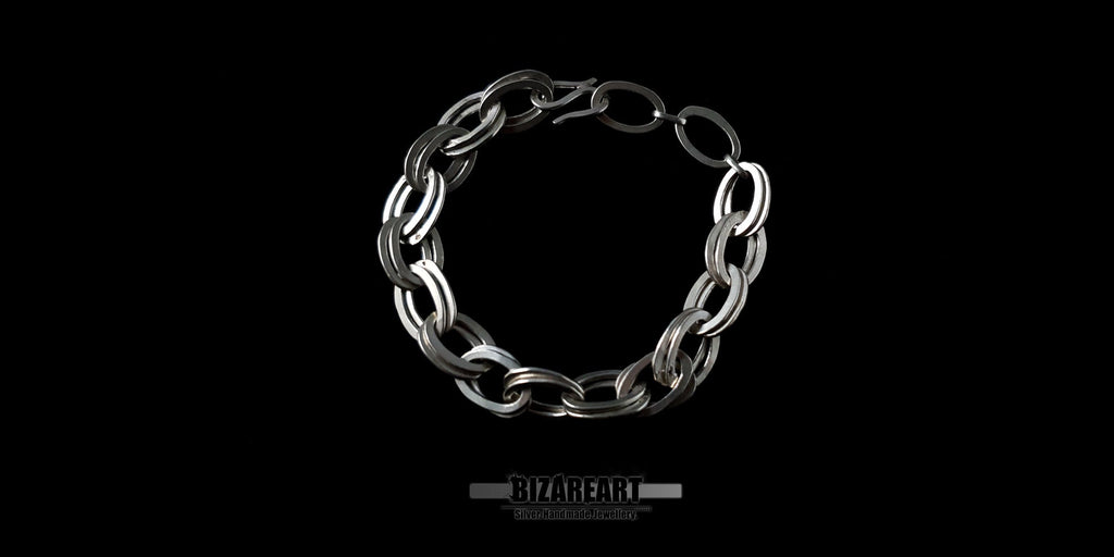 Top-down view of a handcrafted double loop sterling silver chain bracelet with a secure S-hook clasp against a black background.