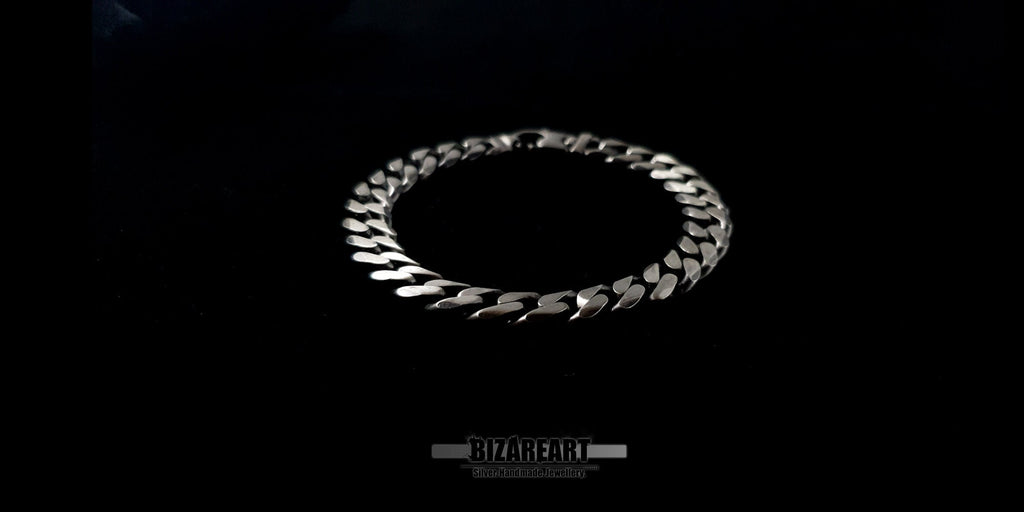 Angled view of a silver Gourmette bracelet showcasing the interlocking flat curb links and reflective metallic finish.