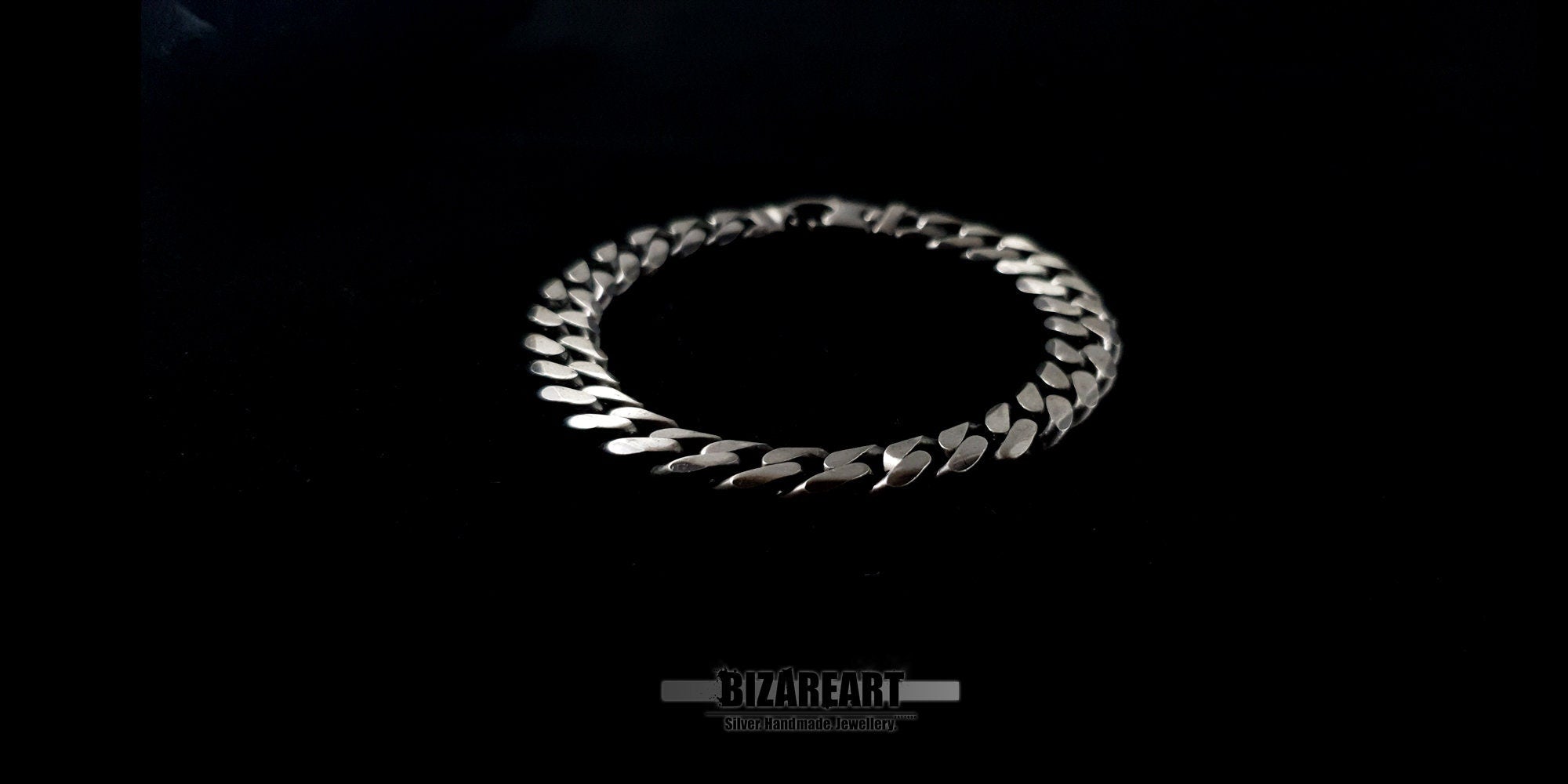 Angled view of a silver Gourmette bracelet showcasing the interlocking flat curb links and reflective metallic finish.