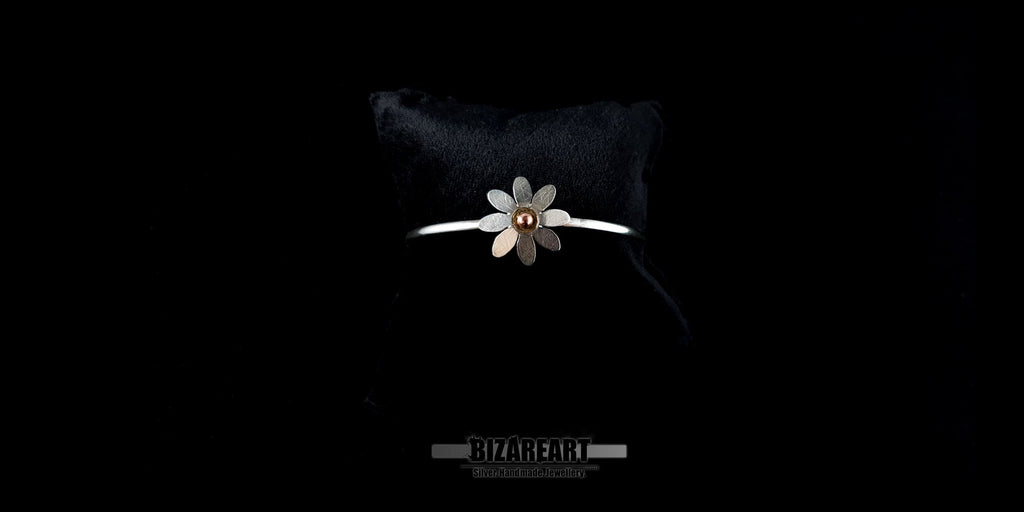 Delicate handmade silver jewelry bangle with a detailed bohemian daisy centerpiece against a dark background.