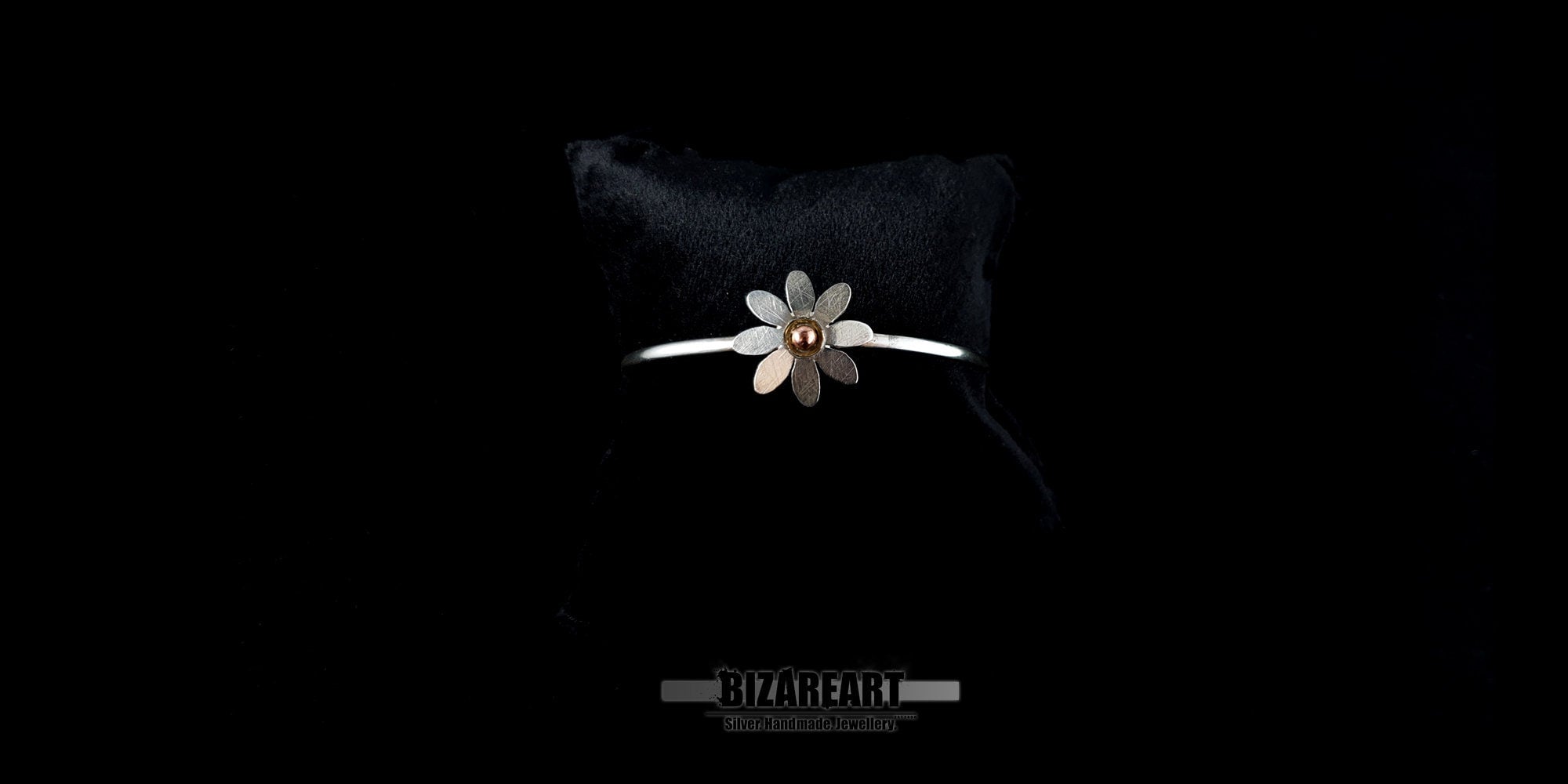 Delicate handmade silver jewelry bangle with a detailed bohemian daisy centerpiece against a dark background.