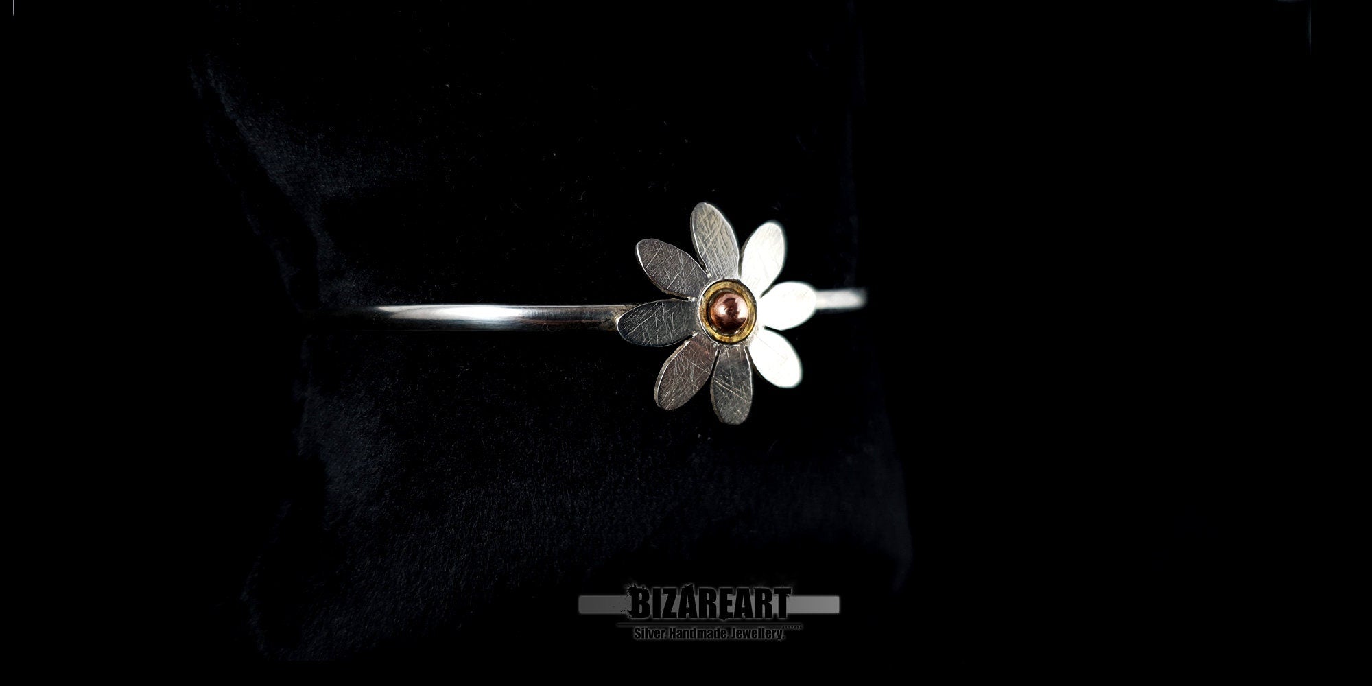 Angled side view of an artisan sterling silver open-cuff bracelet showing the unique handmade craftsmanship.