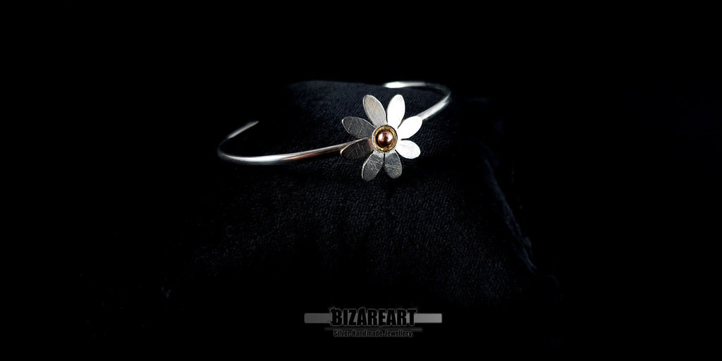 Slanted profile shot of a shiny .925 sterling silver daisy bangle highlighting its sleek wire band and gold-plated accents.
