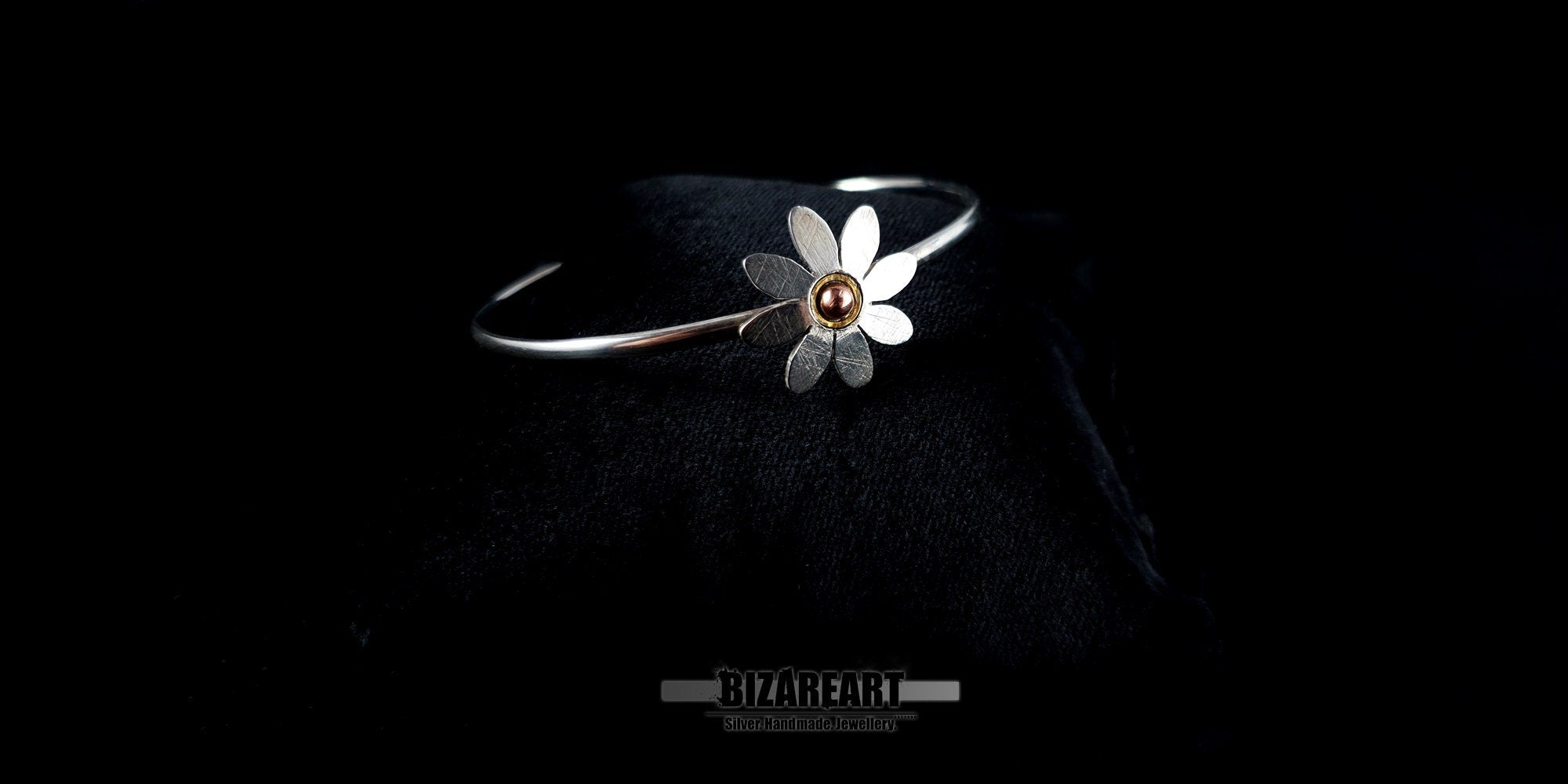 Slanted profile shot of a shiny .925 sterling silver daisy bangle highlighting its sleek wire band and gold-plated accents.