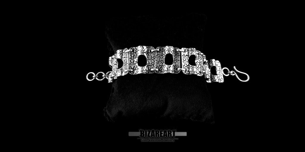 Close-up front view of the detailed silver panel bracelet, showcasing the textured artisan craftsmanship and high-shine finish on a reflective black surface.