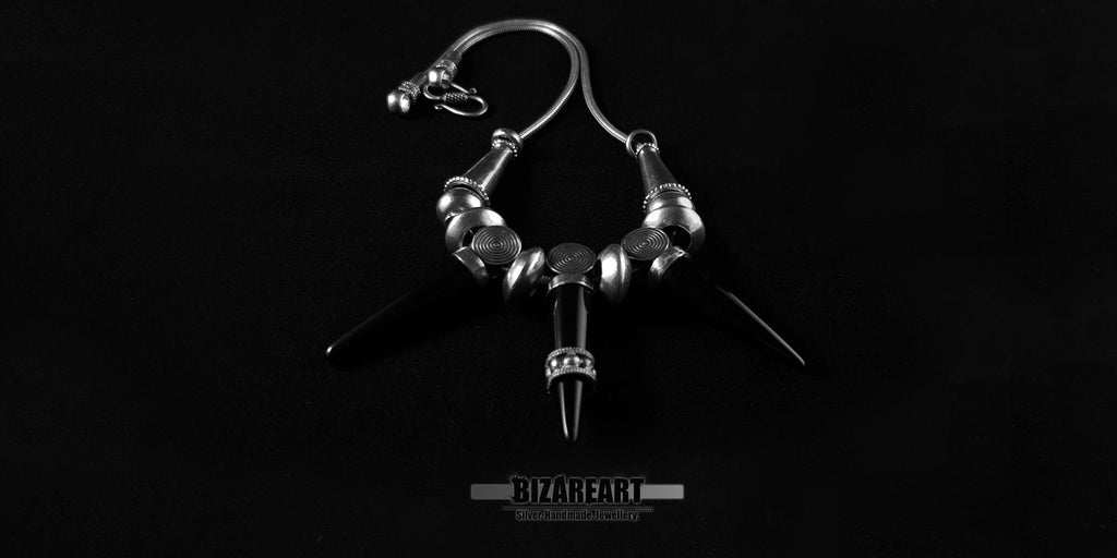 Gothic style silver snake chain necklace with three black onyx cone pendants arranged symmetrically against a black backdrop.