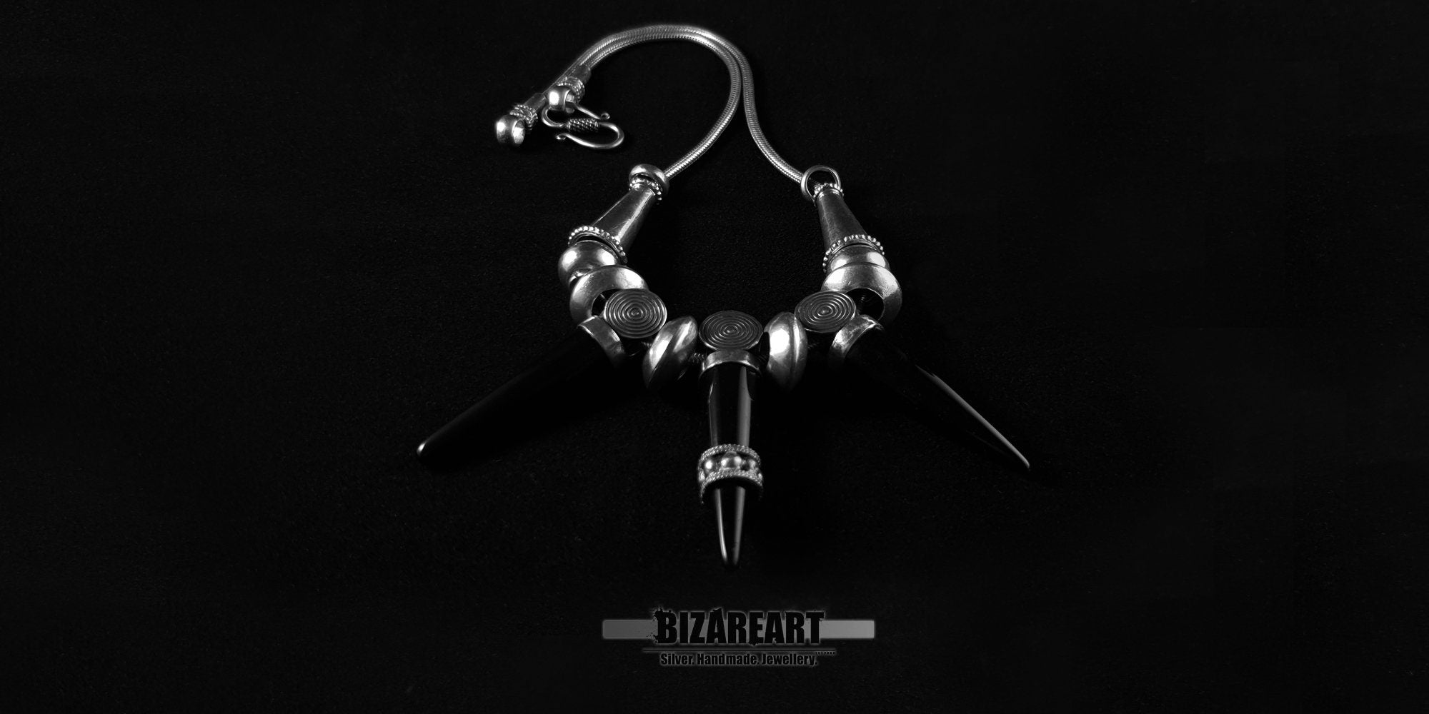Gothic style silver snake chain necklace with three black onyx cone pendants arranged symmetrically against a black backdrop.
