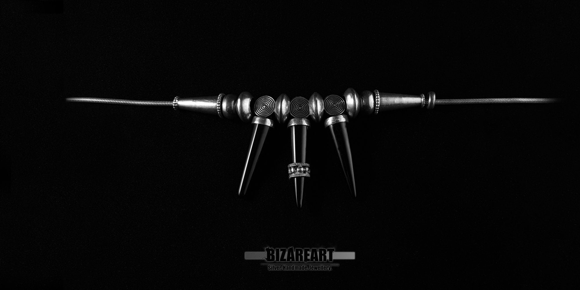 Flat lay presentation of the Bizareart sterling silver gothic necklace with three onyx spikes laid out linearly.