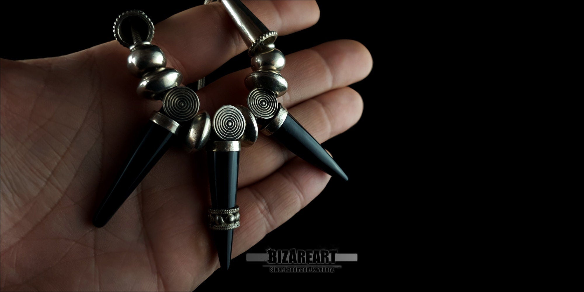 The Black Onyx Elegance Necklace held in a hand to demonstrate the product scale, luxurious weight, and size of the spike pendants.