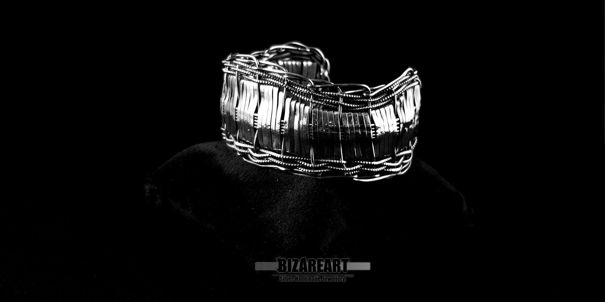 Front-facing macro shot of the silver open section bangle displayed on a display stand, emphasizing the central gauze-style wrap technique.