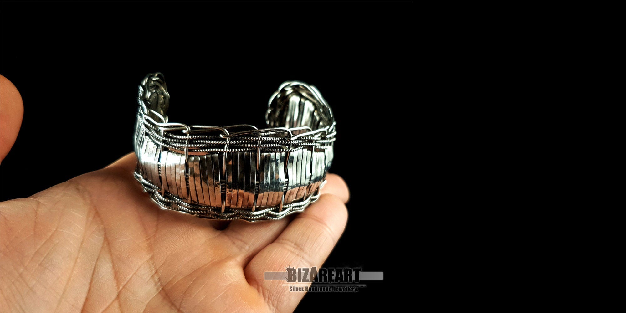 A hand holding the multilayered silver bracelet to show scale, emphasizing its substantial feel and comfortable, smooth curved edges.