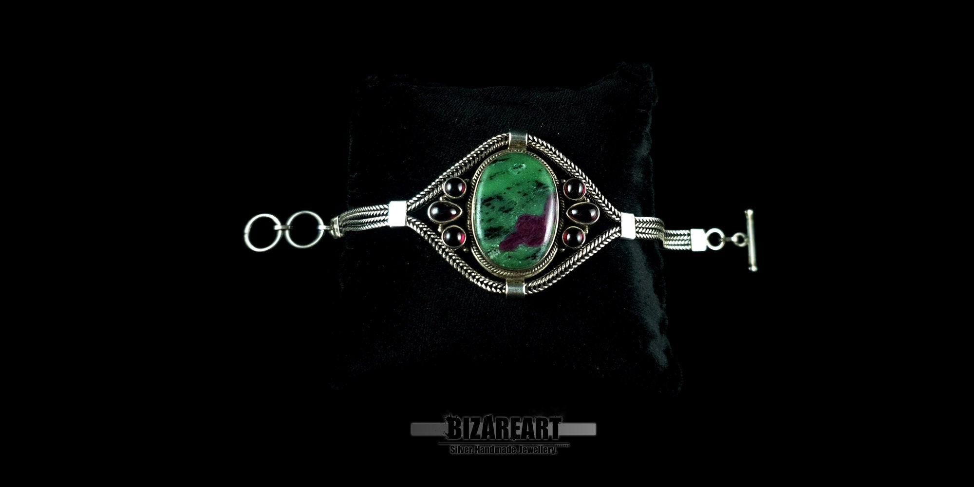 Front view of the oval green and red Ruby Zoisite gemstone bracelet on a black display cushion.