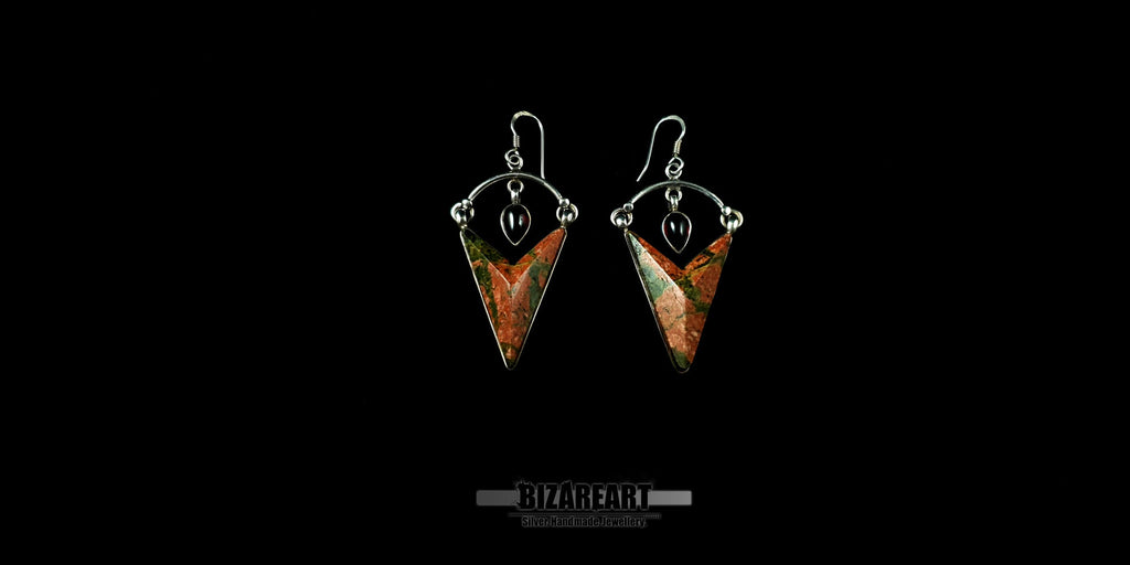 A pair of handmade Unakite earrings displayed centrally on a black background, showing the symmetrical design and the delicate silver arch holding the garnet stone.