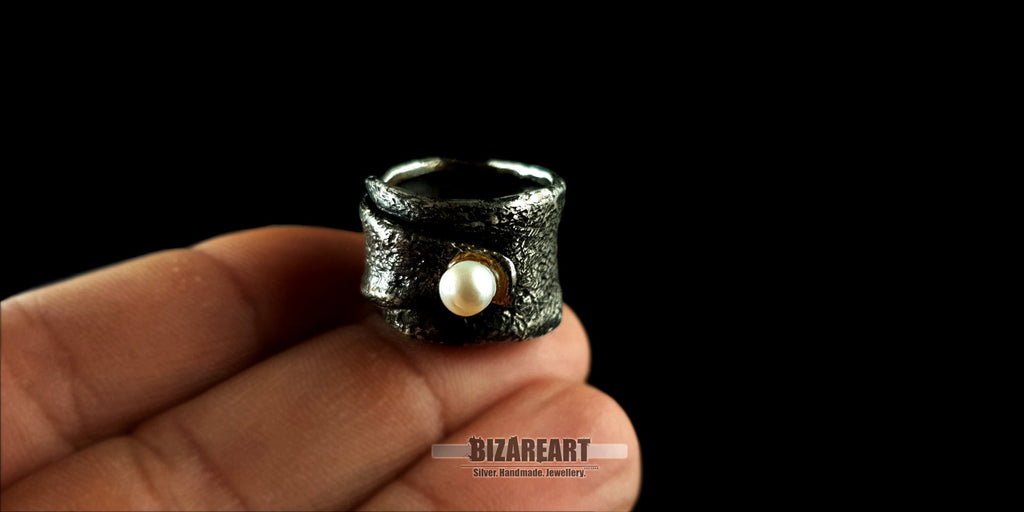 Hand held view brutalist-style oxidized silver ring by Bizareart, showcasing the intricate casted texture and a luminous pearl focal point.