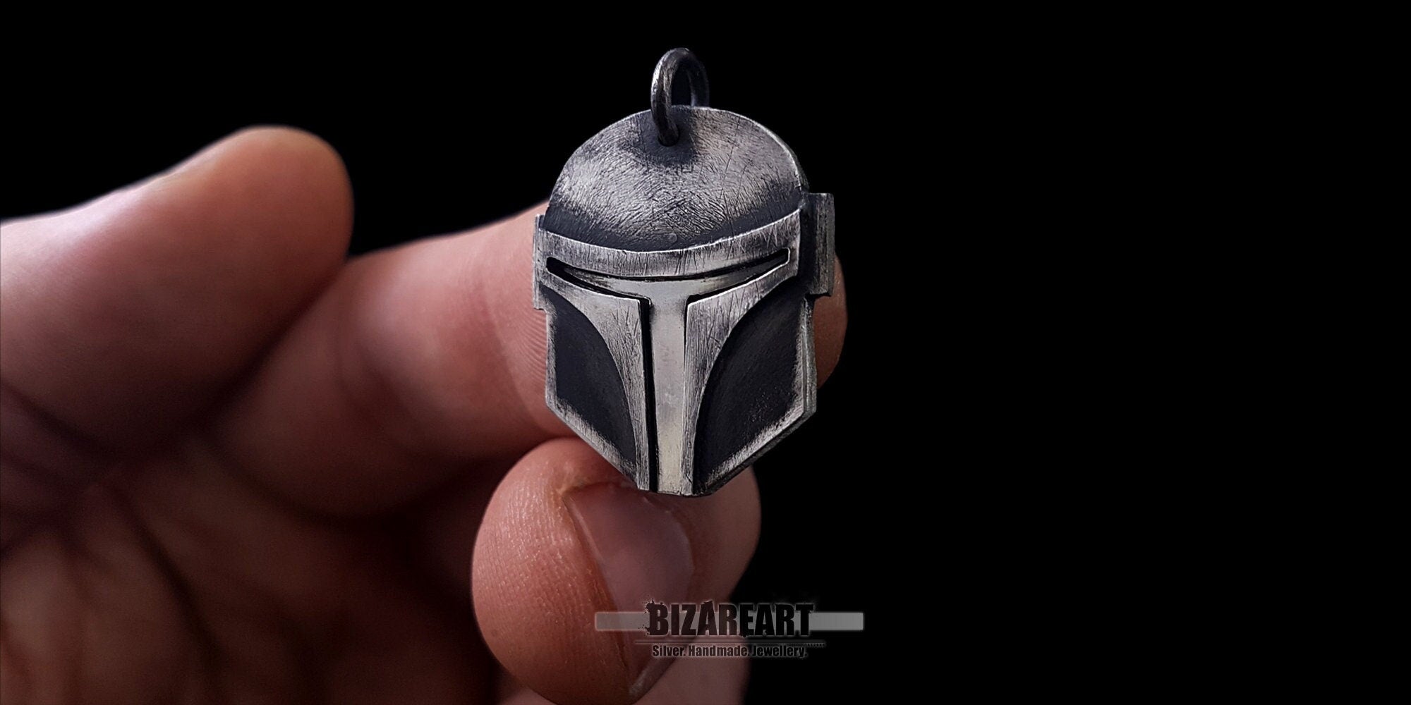 Close-up of the artisan silver Star Wars helmet pendant held between fingers to showcase its scale and craftsmanship.