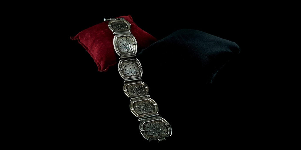 A wide-angle view of the heavy floral engraved silver link bracelet draped elegantly over dark luxury fabric.