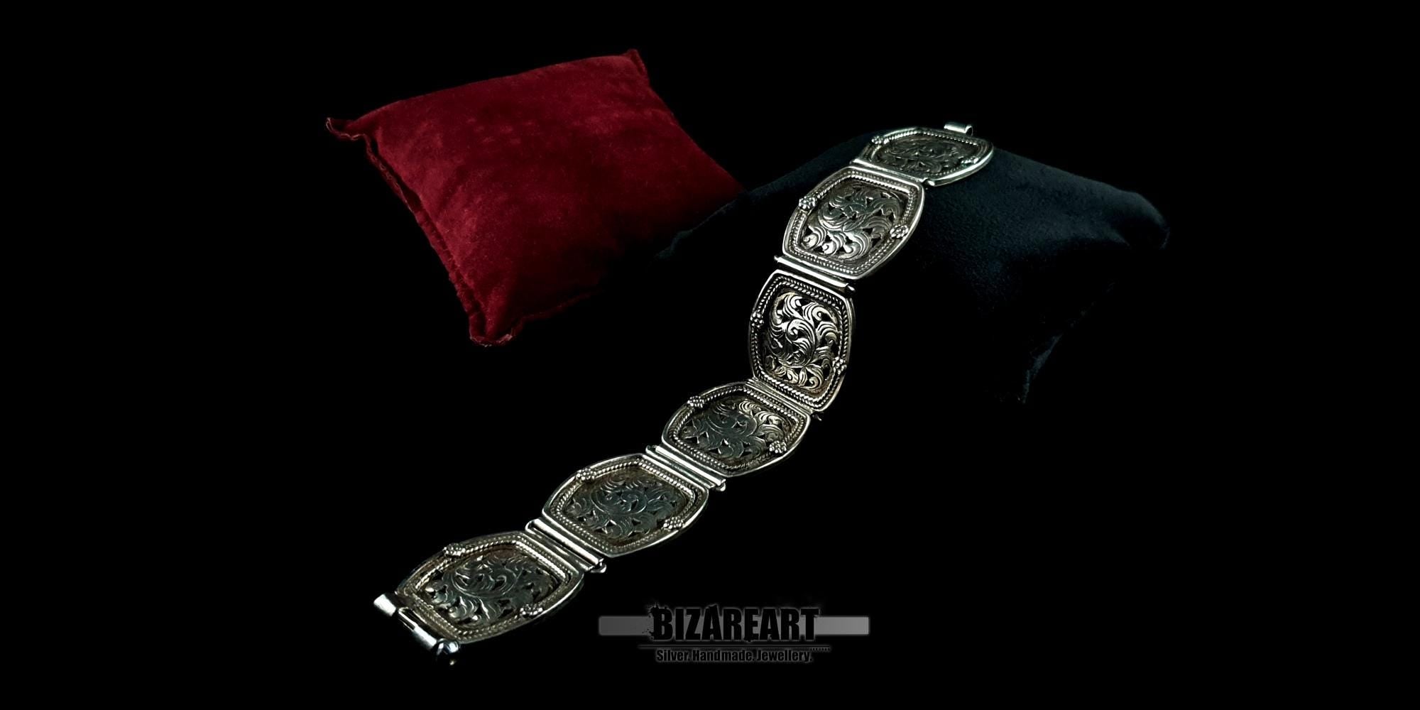 A wide-angle view of the heavy floral engraved silver link bracelet draped elegantly over dark luxury fabric.