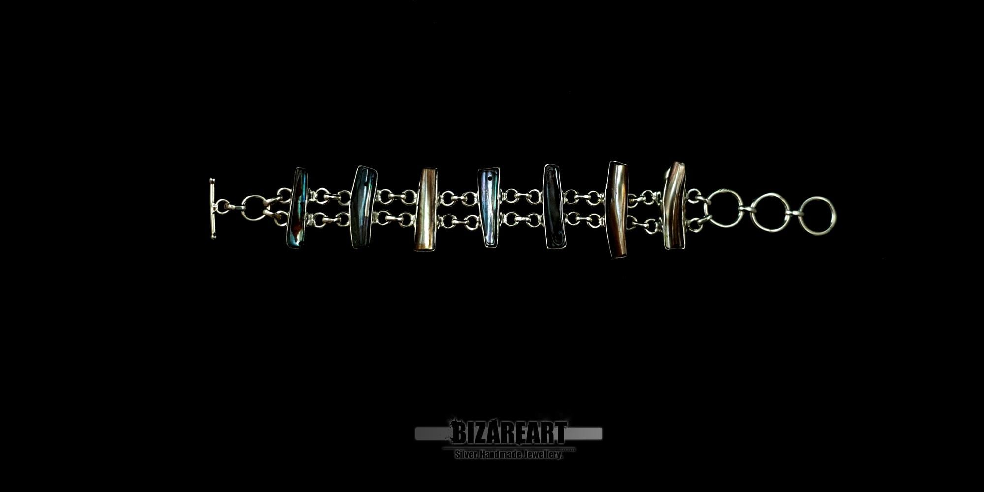 Handmade sterling silver toggle bracelet featuring seven vertical bar-shaped bezel settings with iridescent baroque pearls on a black background.