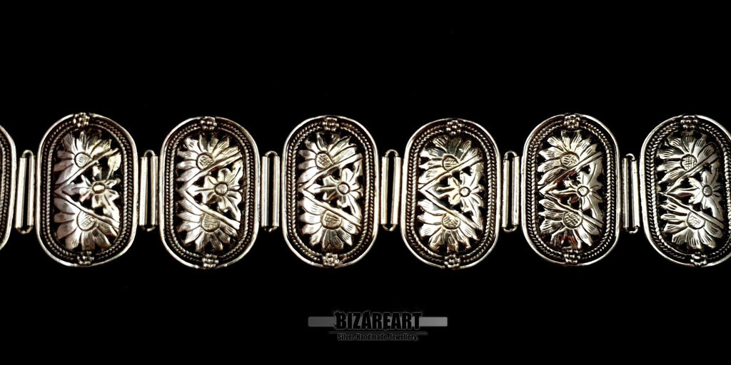 Extreme close-up of the textured, detailed floral engravings on the silver bracelet panels.