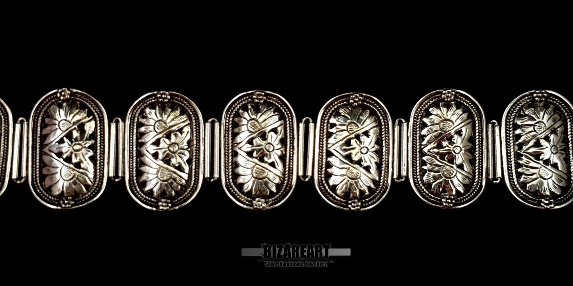 Extreme close-up of the textured, detailed floral engravings on the silver bracelet panels.