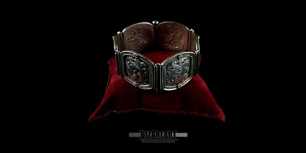 Ornate silver statement bracelet resting on a luxury red velvet pillow, highlighting its substantial thickness and polished finish.