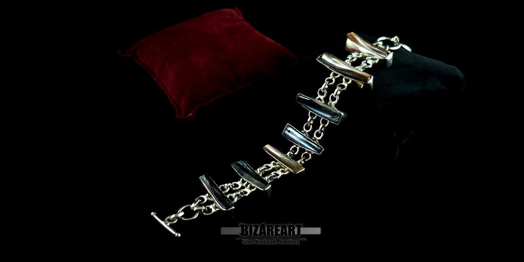 Luxury artisan silver bracelet draped elegantly across a red velvet display cushion under moody, dramatic lighting.