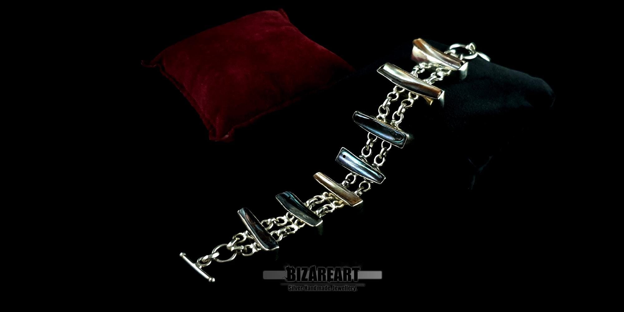 Luxury artisan silver bracelet draped elegantly across a red velvet display cushion under moody, dramatic lighting.