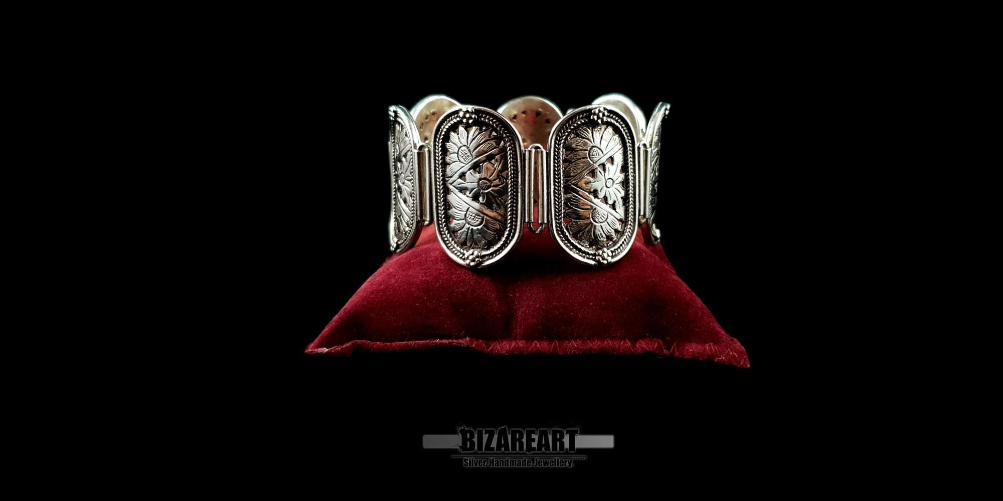 Handcrafted .925 sterling silver statement bracelet with 7 floral panels, displayed on a red velvet cushion.