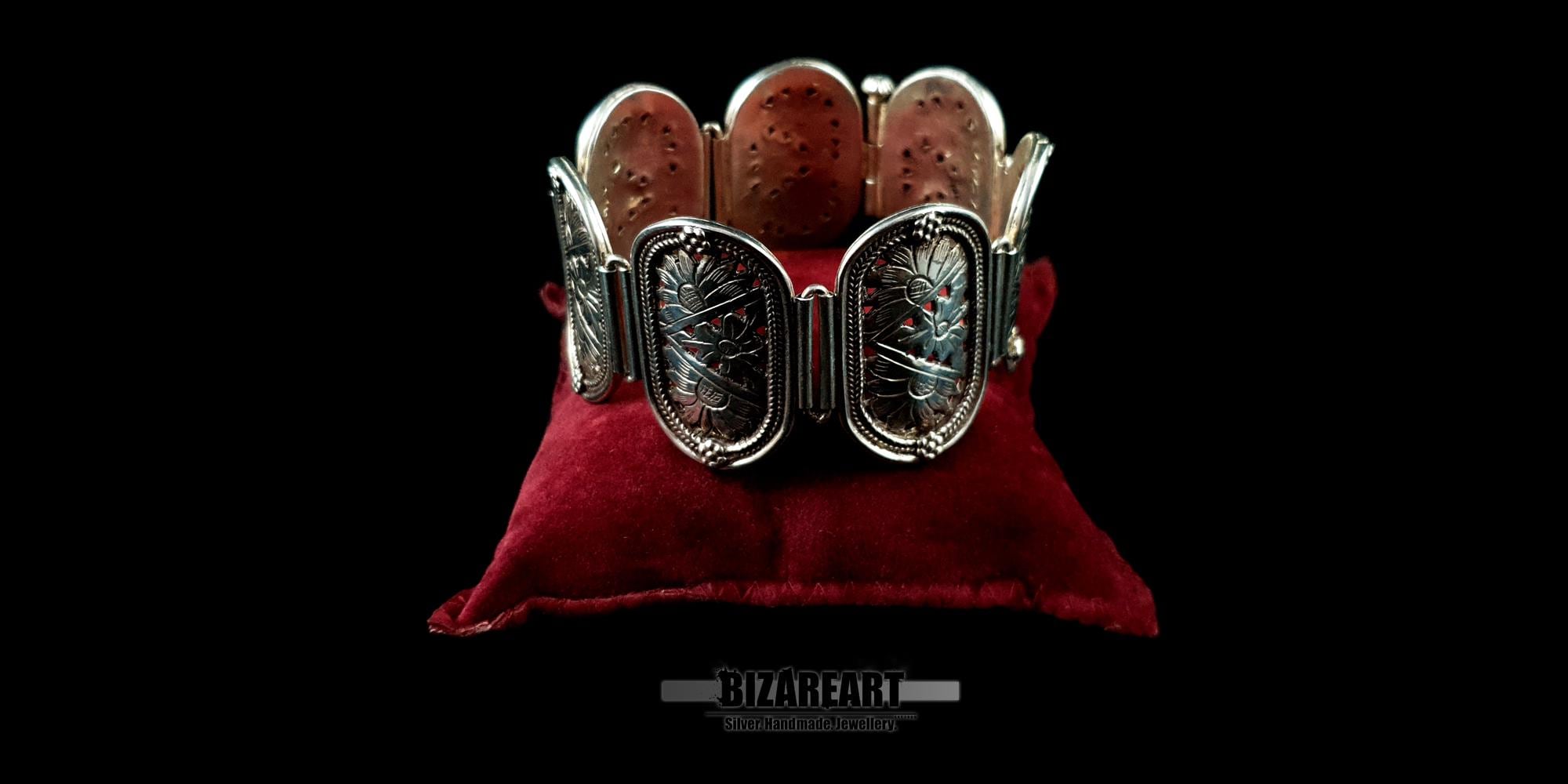 Wide silver engraved cuff bracelet curved and upright on a red velvet pillow, showing its heavy profile.